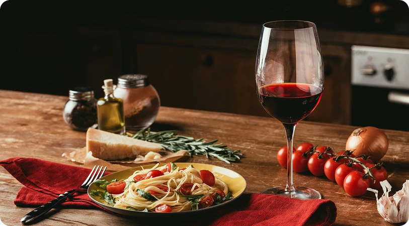 A fotón egy hangulatos, food-fotós stílusú csendélet látható, amelyet a házi konyha meleg és étvágygerjesztő légkörében készítettek. A faasztalon egy tál tészta áll, amelyet cseresznyeparadicsom-félékkel és zöldfűszerekkel díszítettek; mellette egy villa fekszik egy piros szalvétán.